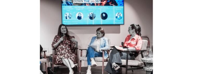 Three white women sit on a panel discussing sustainability and D&I within a business